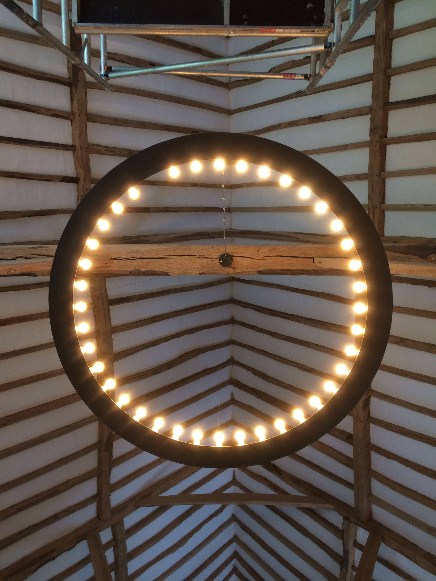 Circular light fitting hanging within a freshly finished timber framed barn